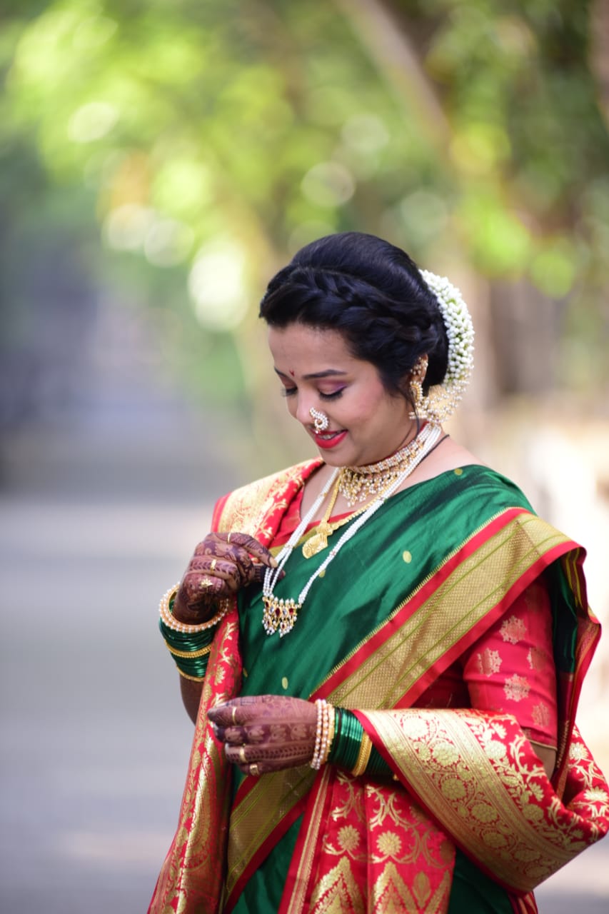 Elegant traditional Indian woman in vibrant green saree with gold and red floral embroidery, wearing intricate jewelry including a nose ring, bracelets, and a necklace, posing in a natural outdoor setting
