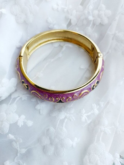 Elegant gold-toned bracelet with intricate purple enamel detailing, displayed on a textured white background.