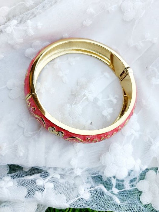 Elegant gold-toned bangle with vibrant red accents, showcased on a white textured surface.