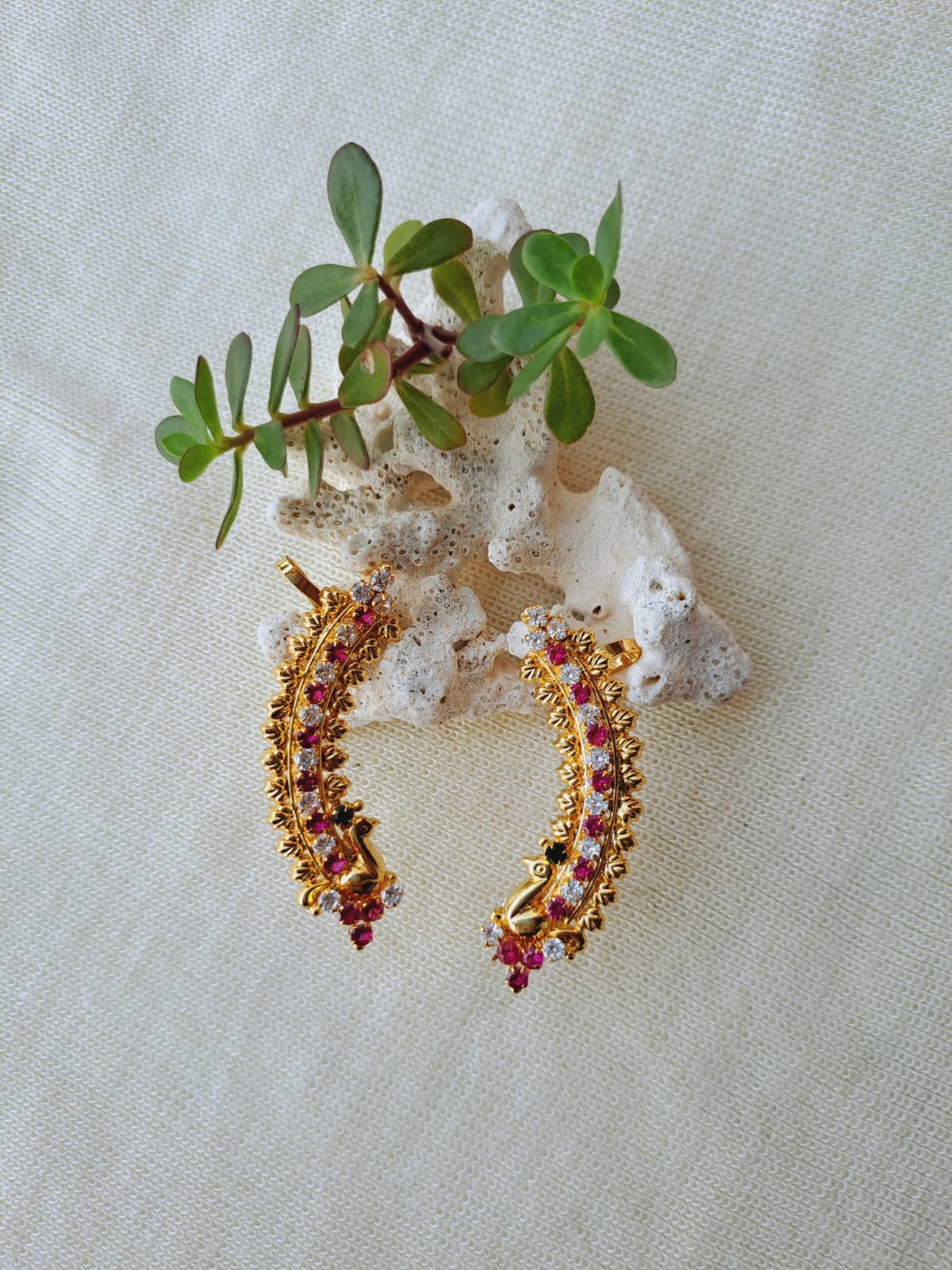 Ornate gold and ruby peacock-inspired kaan design jewelry on a natural floral background