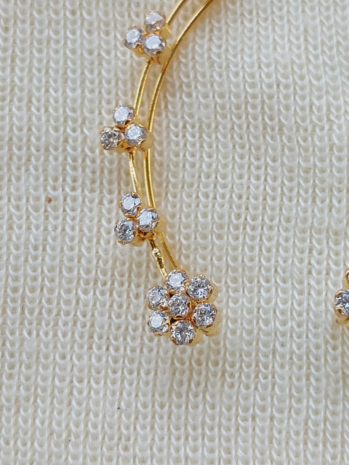 Gold-plated earcuffs adorned with sparkling floral accents, showcased against a textured off-white background.