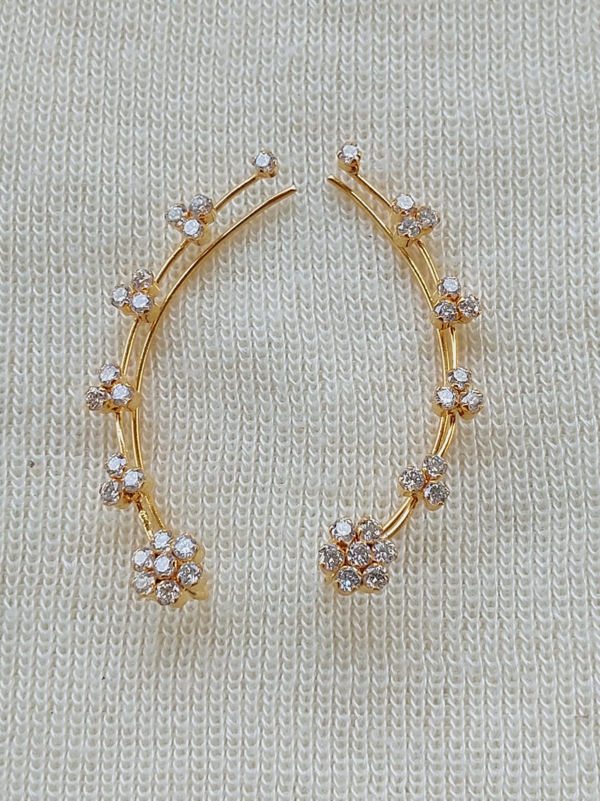 Gold-tone regal earcuffs adorned with sparkling crystals on a cozy knitted fabric background, showcasing a glamorous and elegant jewelry piece from the Mugdha Jewellery Store.