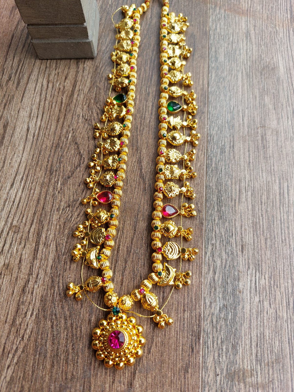 Ornate gold-toned necklace with intricate designs, featuring multicolored gemstones and pendant, placed on a wooden background.