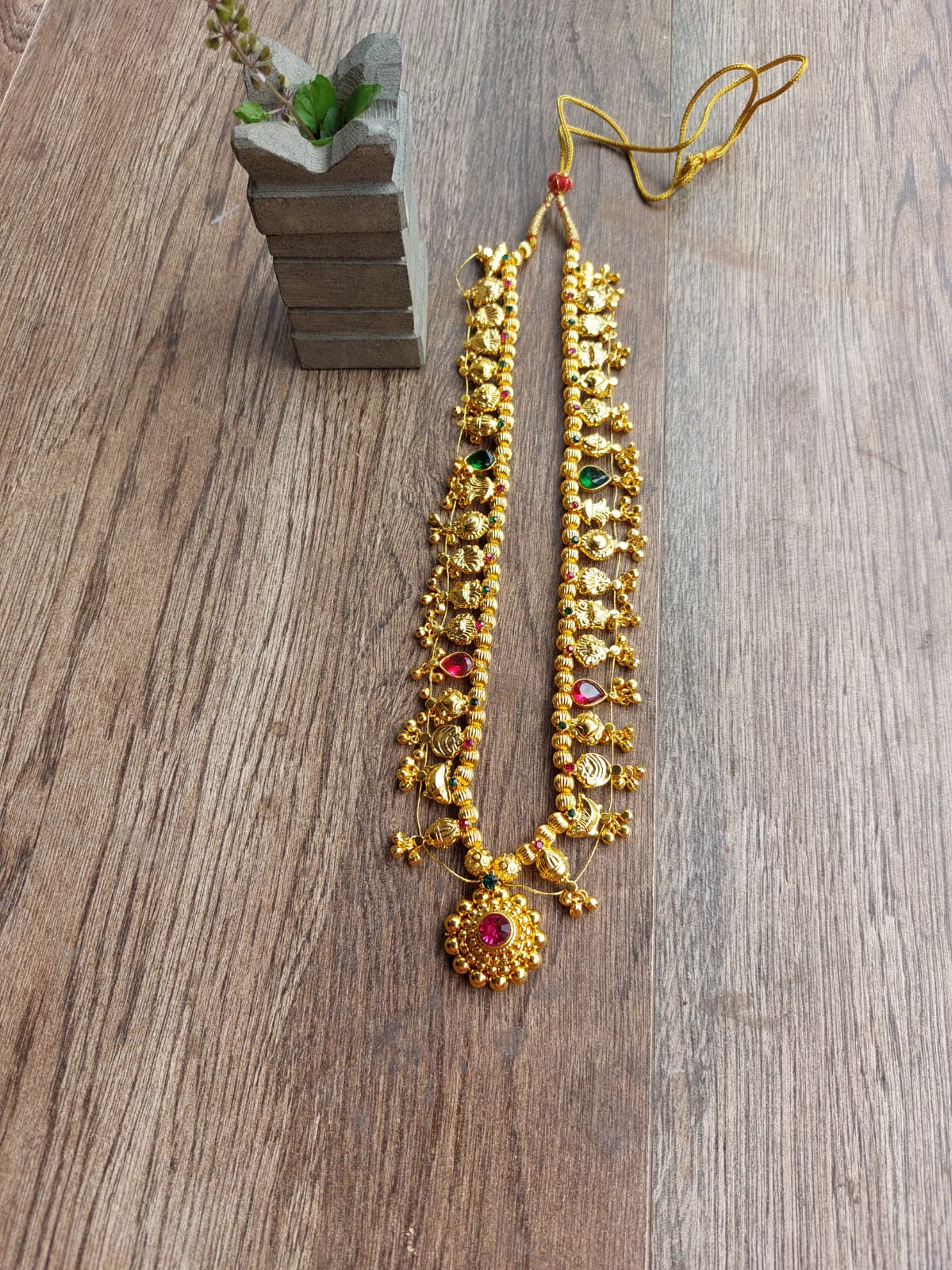 Round bead multicolored heavy Kolhapuri saaj (20 inch) necklace from Mugdha Jewellery Store displayed on a wooden surface with a small plant.
