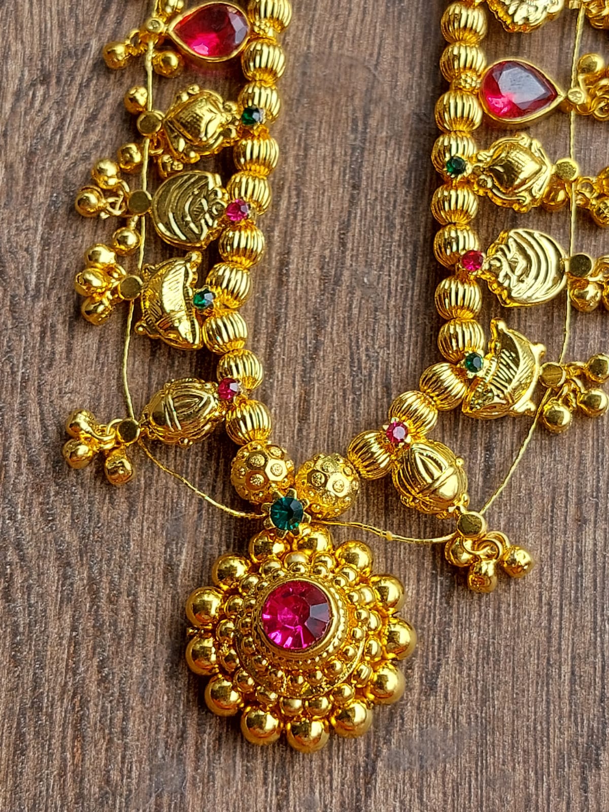 Vibrant gold-tone Kolhapuri saaj necklace with intricate beaded design and radiant gemstone accents against a rustic wooden backdrop from Mugdha Jewellery Store.
