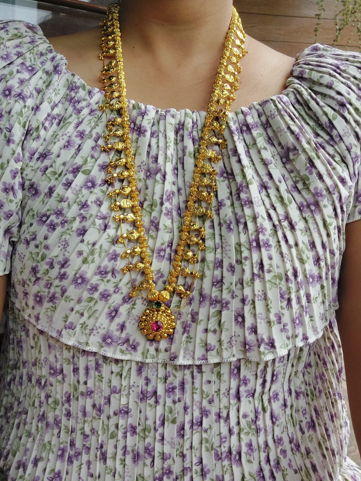 Vibrant floral dress with intricate gold-colored necklace, showcasing a long, striking pendant in the center of the necklace design.