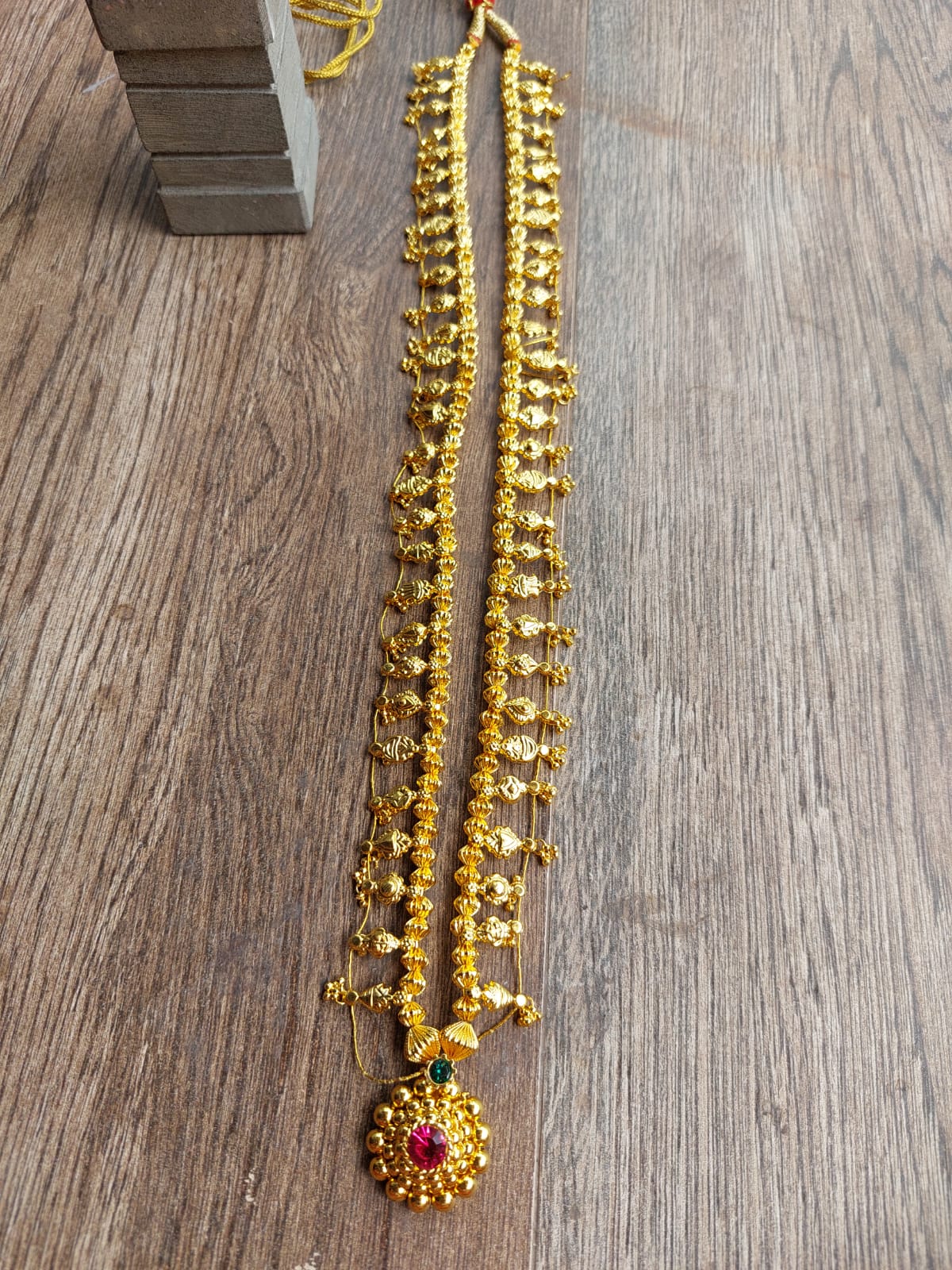 Striking gold-toned jewelry with beaded strands and a central pendant, resting on a wooden surface