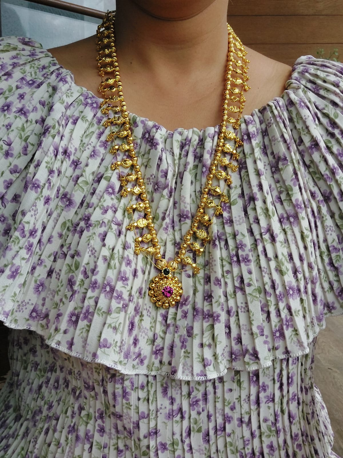 Ornate gold beaded necklace adorns floral patterned purple dress on a person