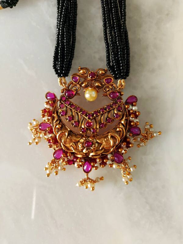 Ornate gold and ruby mangalsutra pendant with multi-strand black beaded chain from Mugdha Jewellery Store.