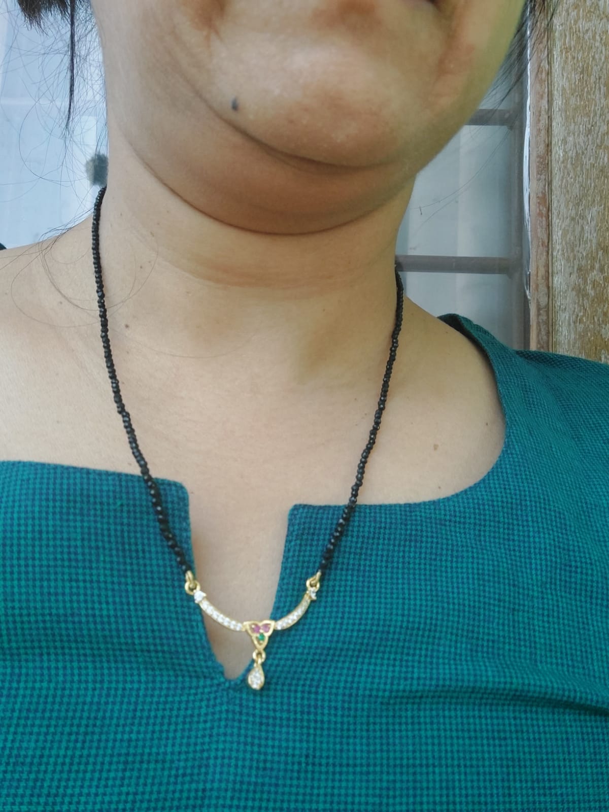 Elegant crystal mangalsutra necklace with delicate teardrop pendant displayed on a person's neck against a teal background.