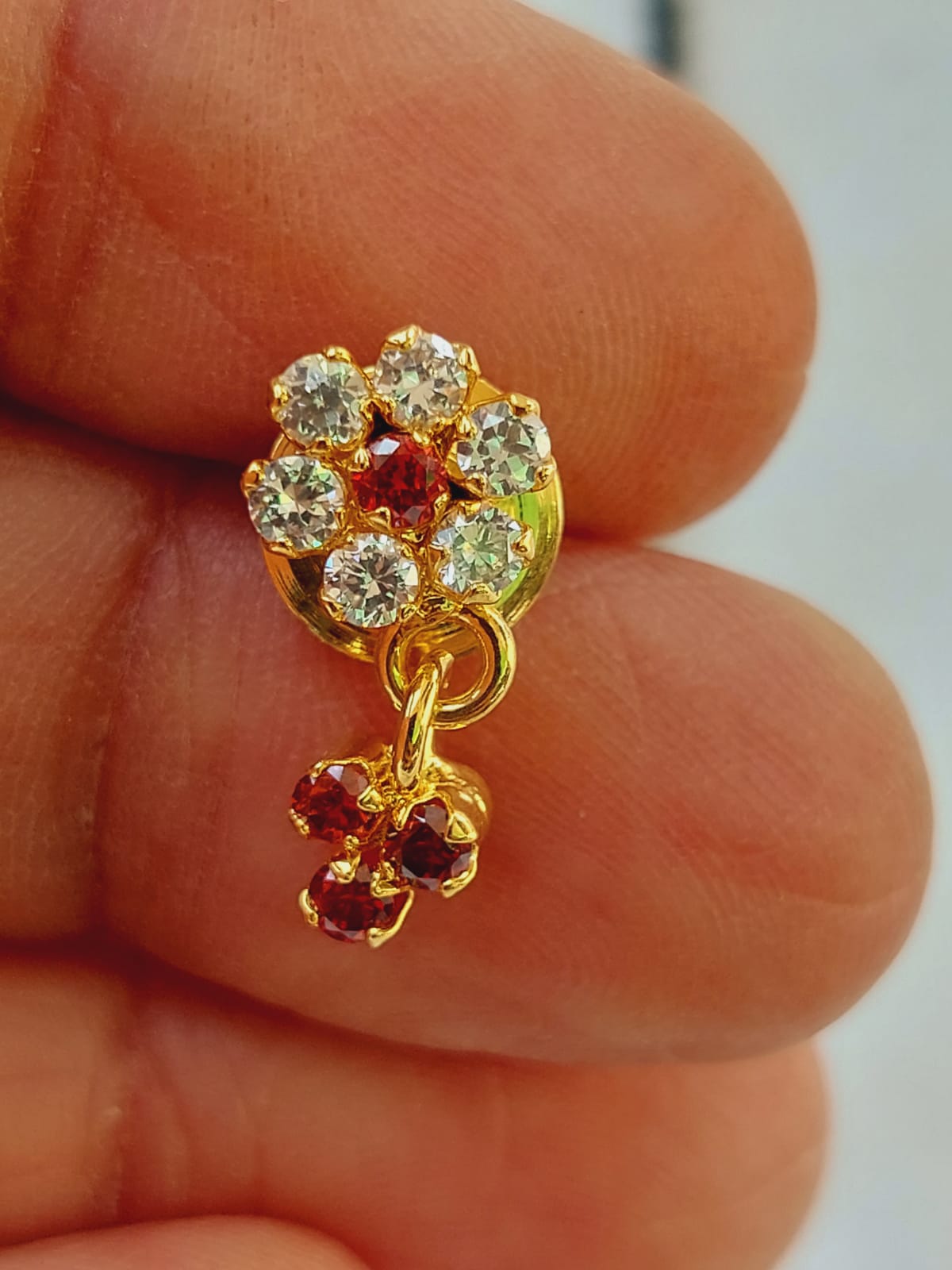 Elegant flower-shaped crystal mangalsutra pendant in gold tone, adorned with vibrant orange and yellow stones, showcased on a person's finger.