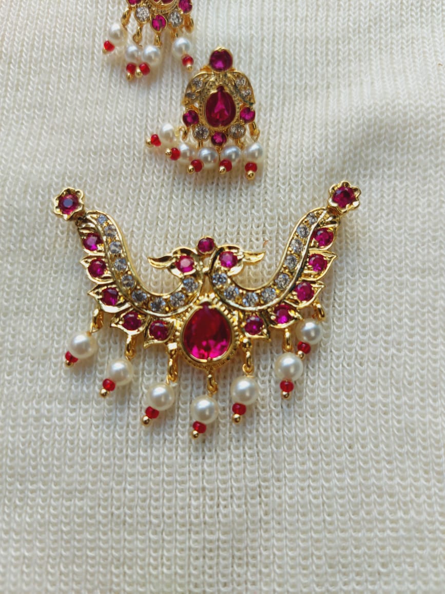 Elegant gold-toned peacock-shaped pendant mangalsutra with vibrant red gemstones and pearly accents, displayed on a white textured background.
