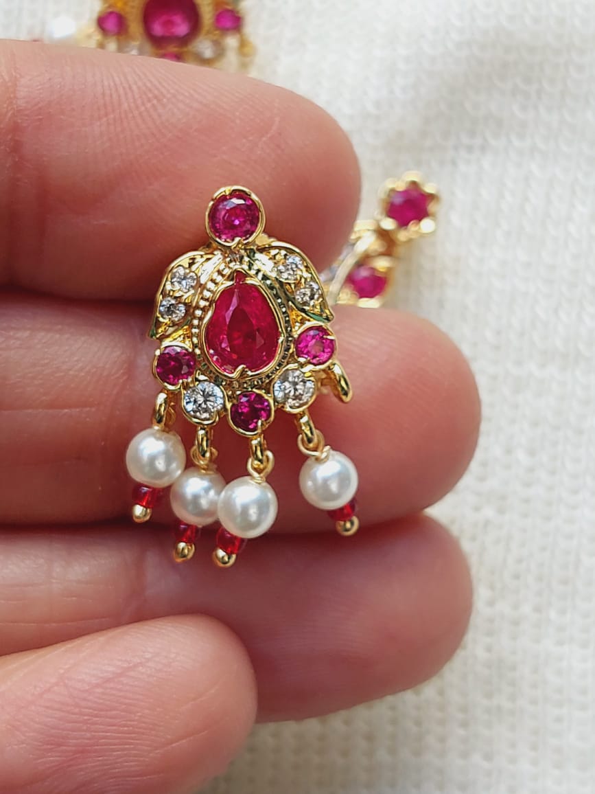 Elegant gold pendant with red gemstone and white pearls on a hand