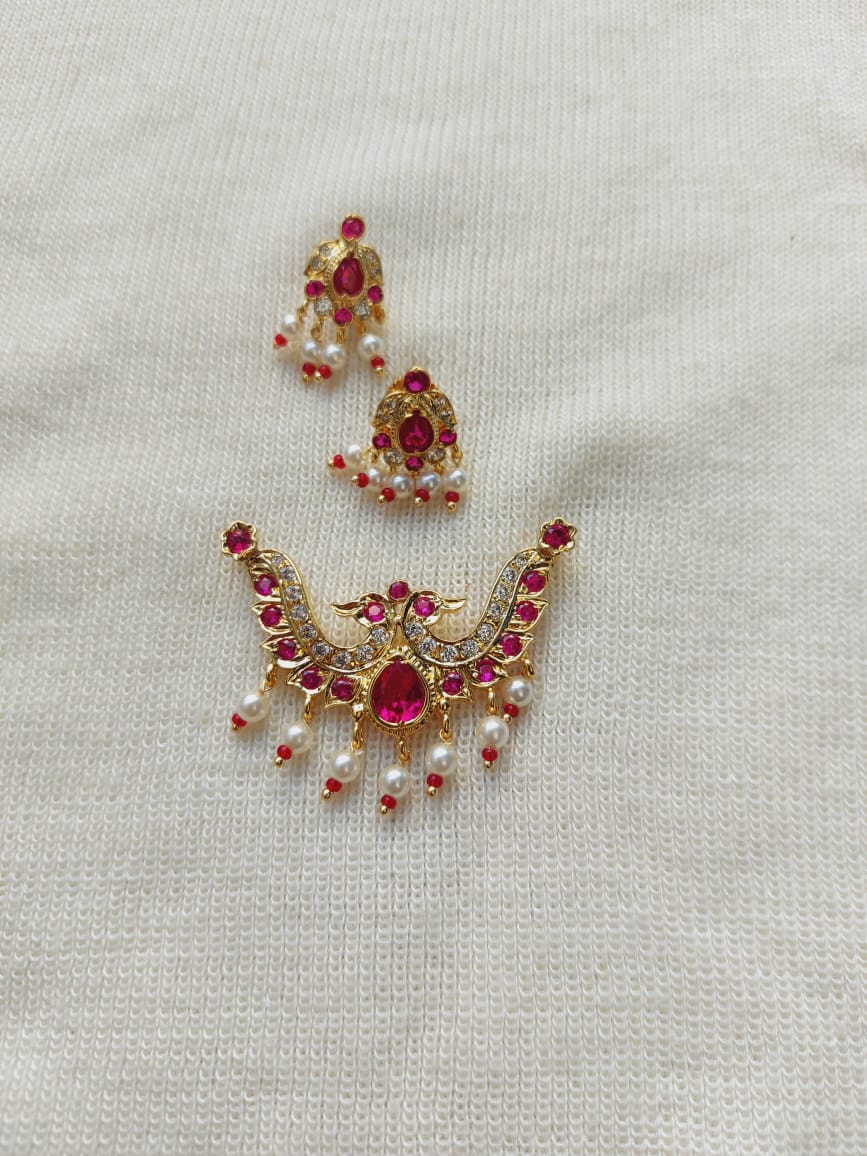Elegant peacock-shaped designer mangalsutra pendant with red gemstones and pearl accents, showcased on a light-colored fabric background.
