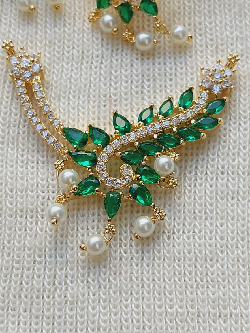 Green and gold designer pendant mangalsutra with glittering emerald-shaped stones and lustrous pearls on a textured white background.