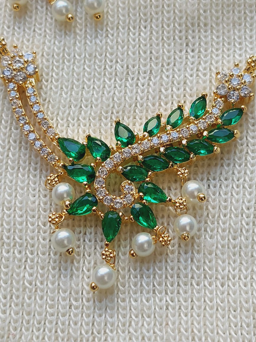 Elegant gold-toned designer pendant with lush green gemstones and lustrous pearls, set against a textured white background.