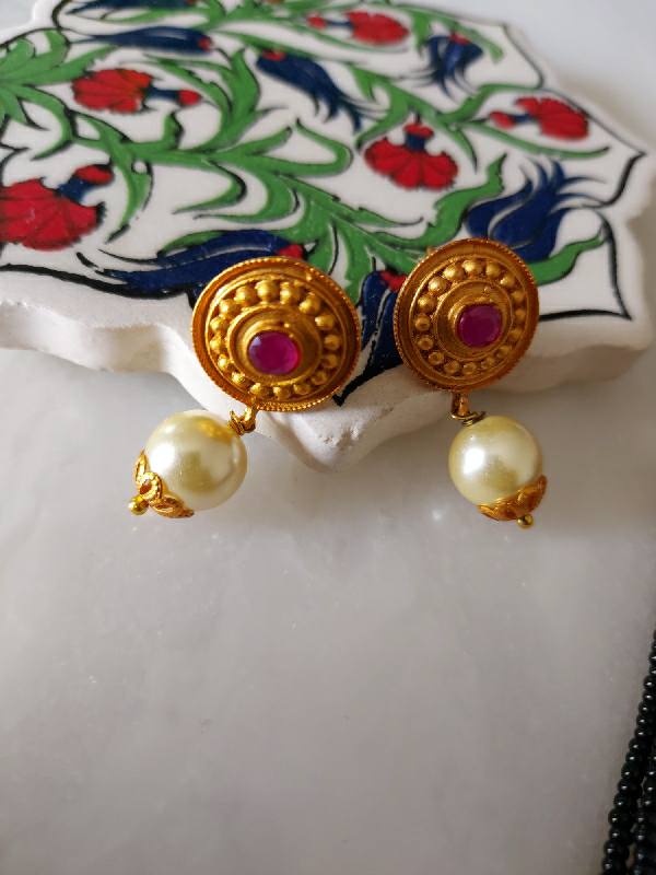 Ornate gold earrings with rubies and pearls on a vibrant floral background from Mugdha Jewellery Store.