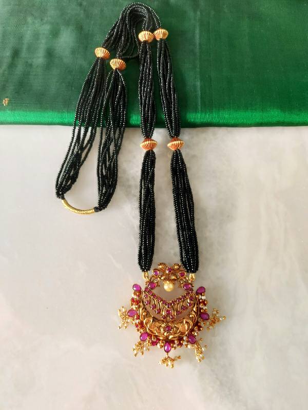 Royal Long Mangalsutra from Mugdha Jewellery Store featuring elegant black beaded strands and an ornate gold and ruby pendant on a white background.