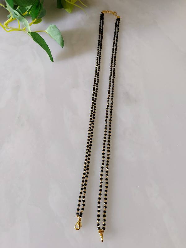 Long, elegant mangalsutra necklace with black beaded strands and gold fish hooks, showcased on a plain white background with a few green leaves.