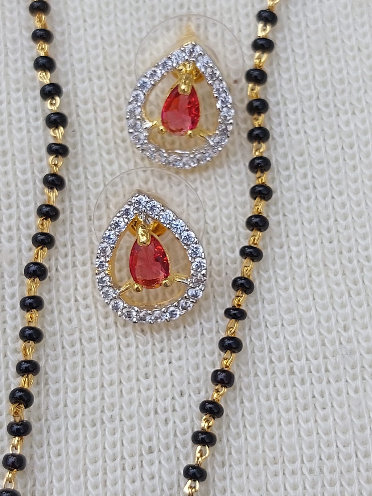 Red Stone Short Mangalsutra - Elegant gold-toned necklace with red gemstone and black bead accents, displayed on a light-colored knitted surface.