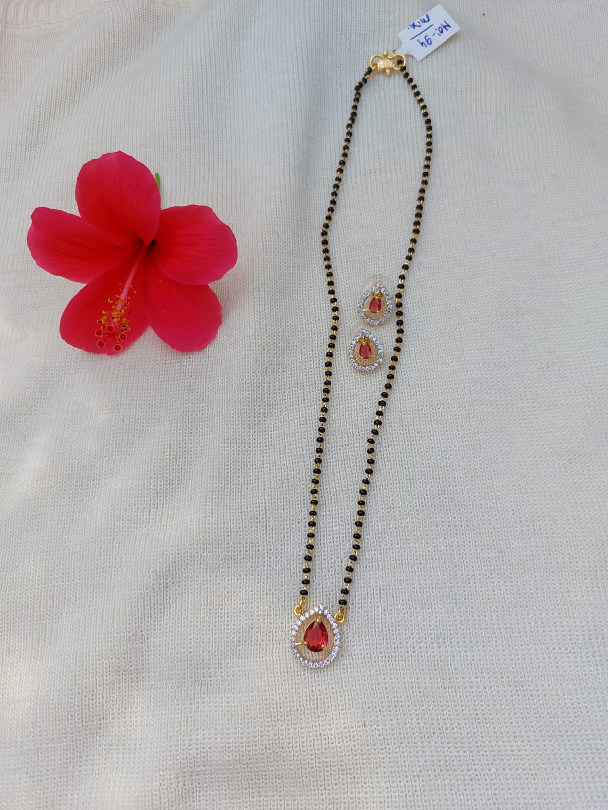 Red stone short mangalsutra with gold chain and pendant on white background with red flower