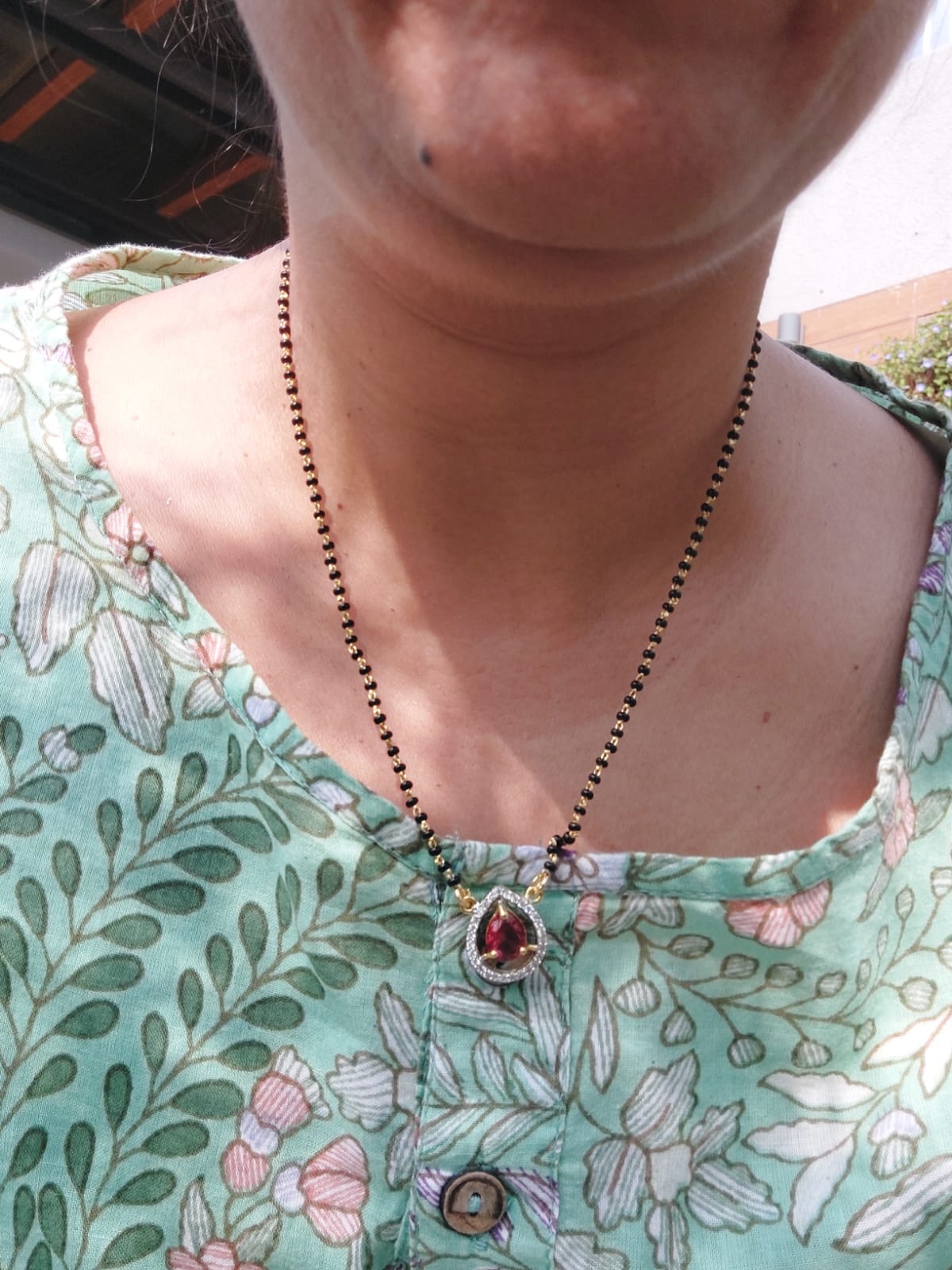 Red Stone Short Mangalsutra - Traditional Indian necklace with red gemstone pendant on beaded chain, worn by person in floral patterned clothing.