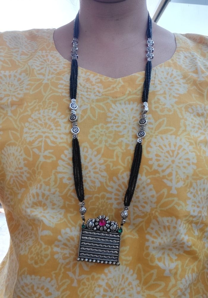 Square Pendant Designer Oxidised Long Mangalsutra featuring intricate patterns, vibrant gemstones, and a stylish pendant against a yellow floral backdrop.