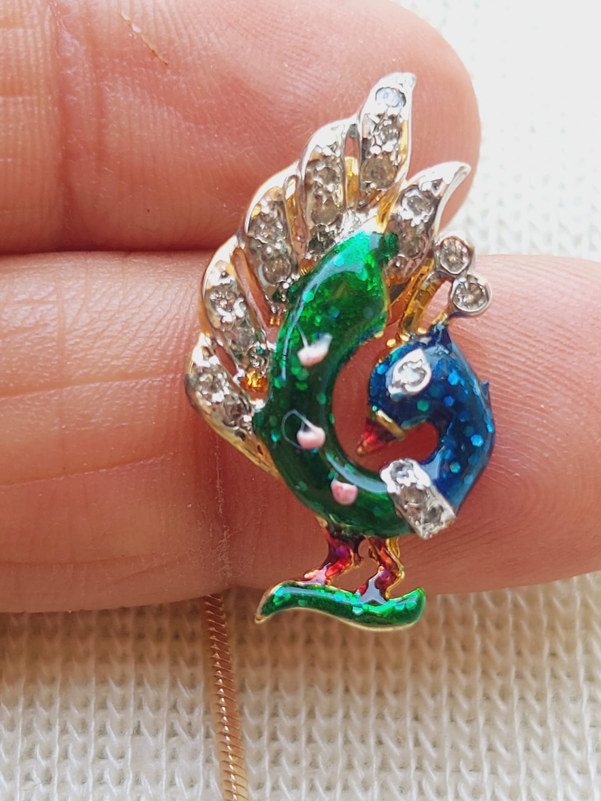 Colorful peacock-themed jewelry piece with rhinestone embellishments and a designer chain, showcased in the image.