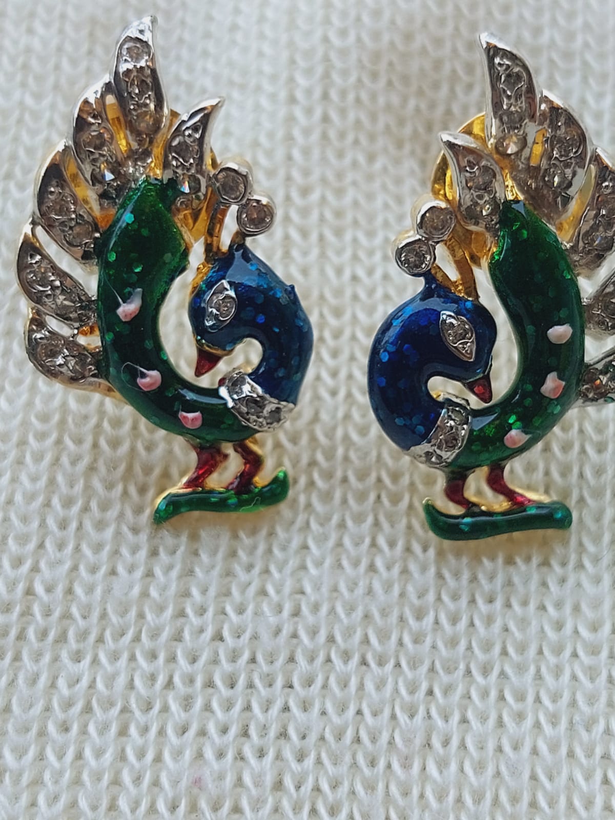 Stunning Meenawork Peacock Set with Designer Chain
Detailed peacock-shaped earrings featuring intricate multicolored enamel work and sparkling rhinestones, showcased on a light-colored knit fabric.
