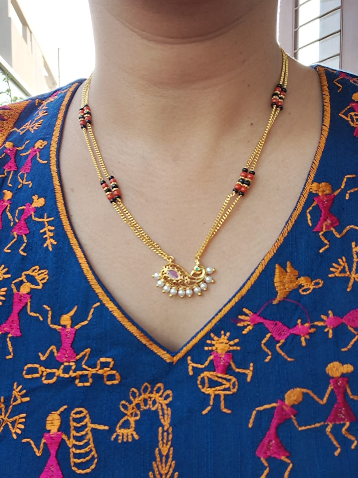 Designer Short Peacock Coral Mangalsutra with ornate gold-toned chain and colorful embroidered floral patterns on the textile backdrop.