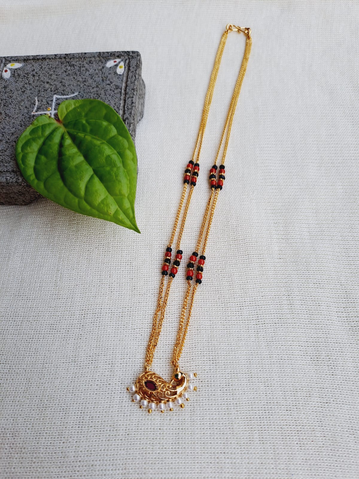 Designer short peacock coral mangalsutra with gold chain and pearl accents on a white background with green leaf decor.