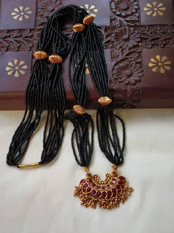 Intricate black beaded mangalsutra with ornate gold and ruby pendant on display at Mugdha Jewellery Store