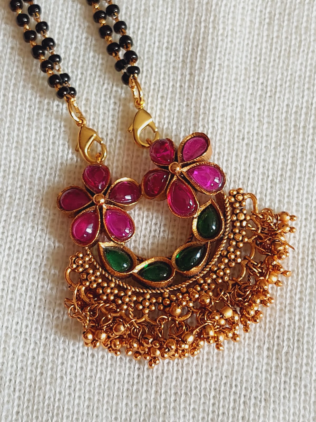 Elegant floral pendant necklace with vibrant gemstones and intricate gold filigree design, displayed on a plain background.