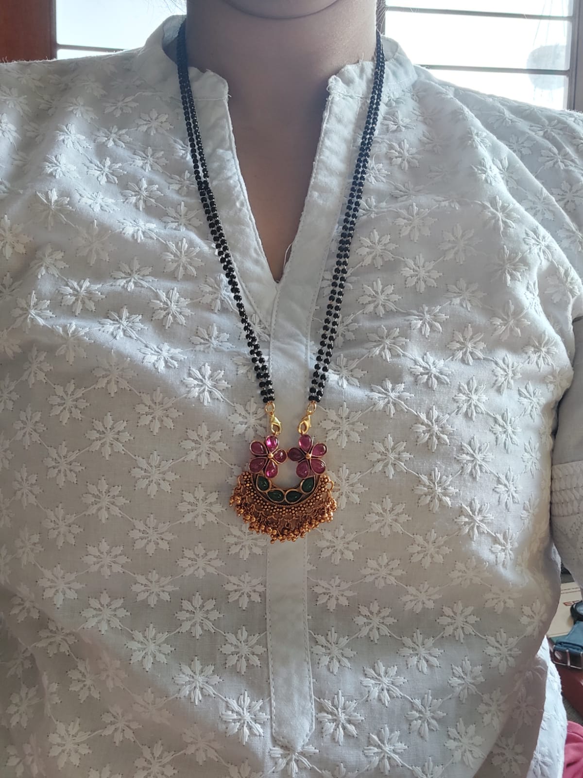 Elegant black and gold designer mangalsutra pendant on a woman's white embroidered kurta.