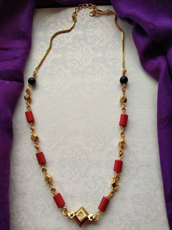 Round Beads Kashithali Short Necklace: Gold-toned necklace with red and black beads, displayed on a white and purple fabric background.