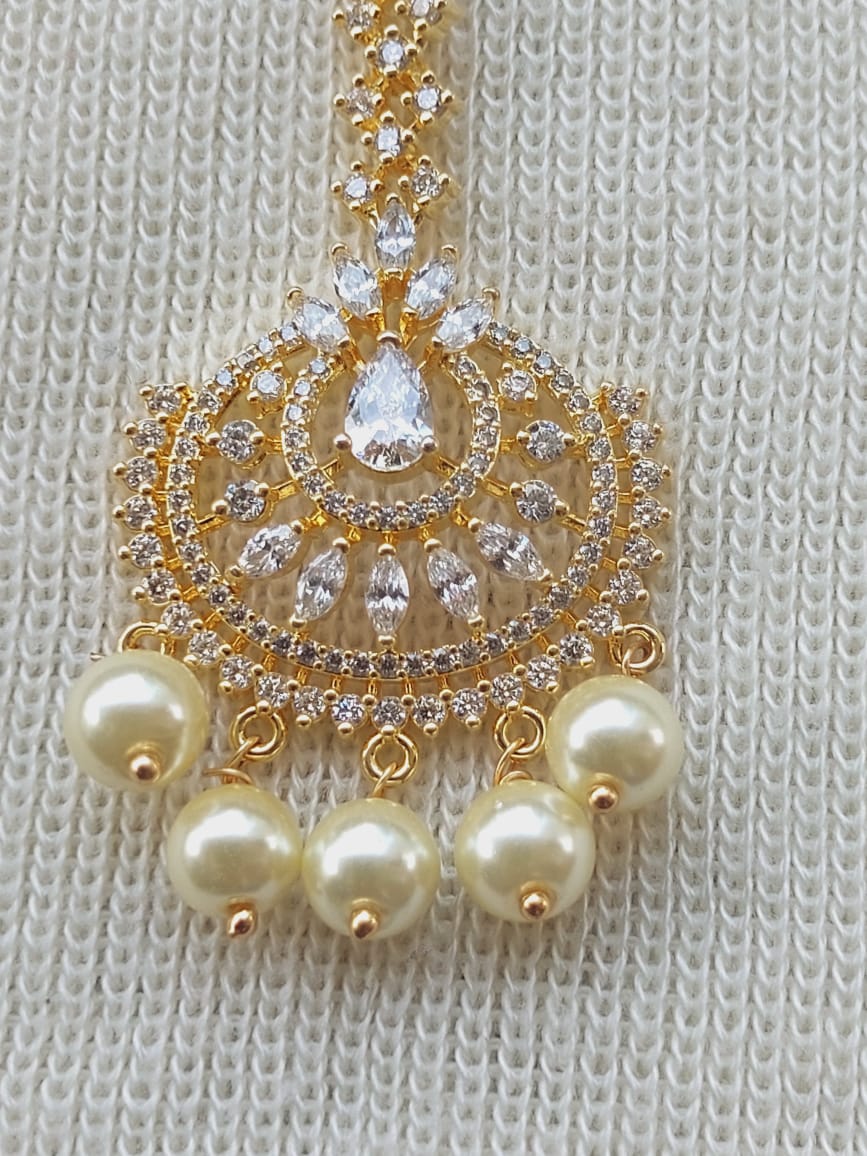 Elegant gold-toned maang tika with intricate floral design adorned with sparkling white stones and lustrous pearl accents.