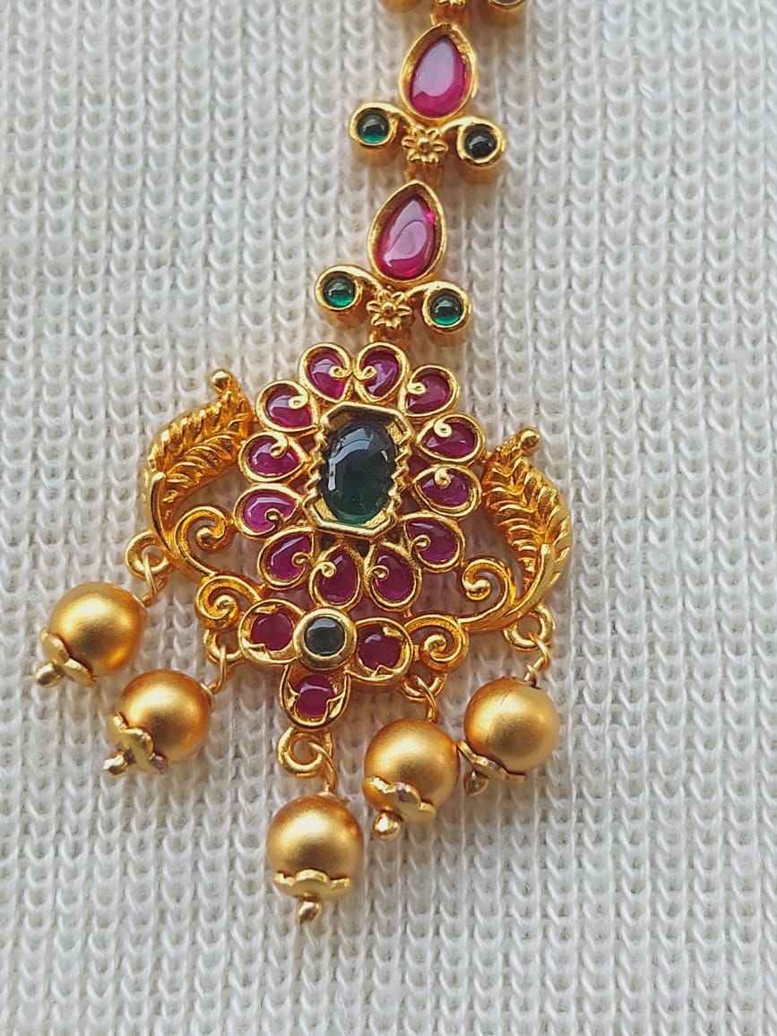 Antique Royal Maang Tika with ornate gold floral design, featuring vibrant ruby and emerald gemstones arranged in a captivating pattern, adorned with intricate golden beads.