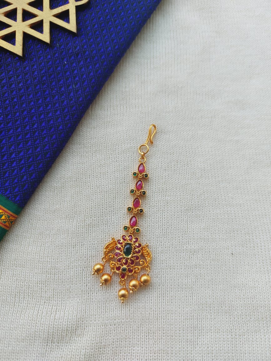 Antique gold and gemstone maang tika with intricate floral design on white and blue background