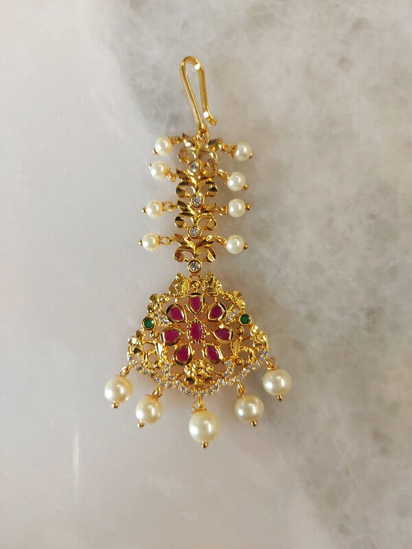 Elegant gold-tone maang tika adorned with sparkling diamonds and rubies, accented with delicate pearl drops.