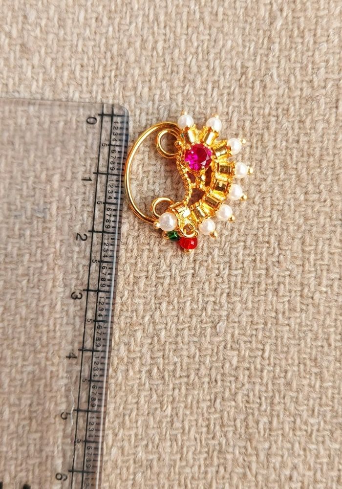 Elegant gold-tone nath with vibrant red and yellow gemstones, pearl accents on neutral fabric background