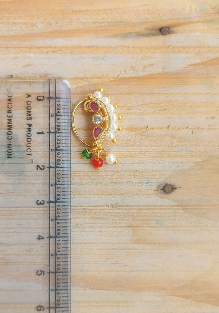 Elegant gold nose ring with ruby-colored gems and pearls, set against a wooden background with a ruler for scale