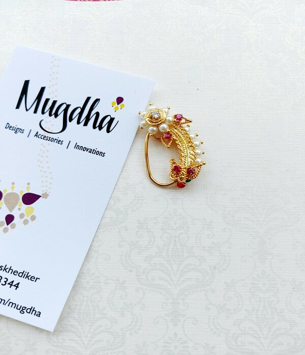 Elegant gold-toned flower-shaped Kashibai nath from Mugdha Jewellery Store, featuring intricate floral patterns and vibrant red accents.