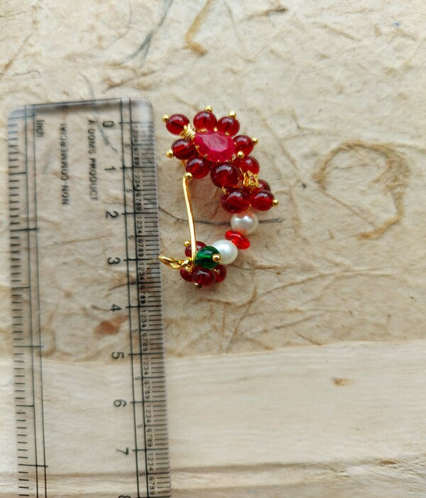 Vibrant Red Floral Nath Nose Ring with Gemstones
This captivating image showcases a traditional Indian nose ring, or "Nath", featuring a striking floral design adorned with vibrant red gemstones. The nose ring is placed on a ruler for scale, highlighting its intricate and ornate craftsmanship.