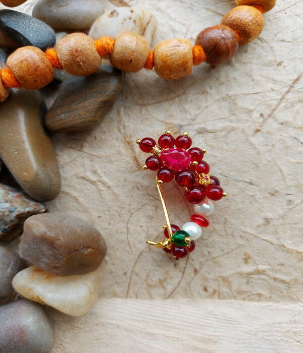 Decorative gold pin adorned with red gemstones, surrounded by natural stone accents on a wooden surface.