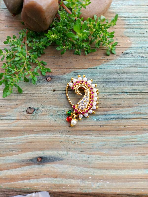 Ornate golden peacock nath with colorful stones on wooden background surrounded by fresh greenery