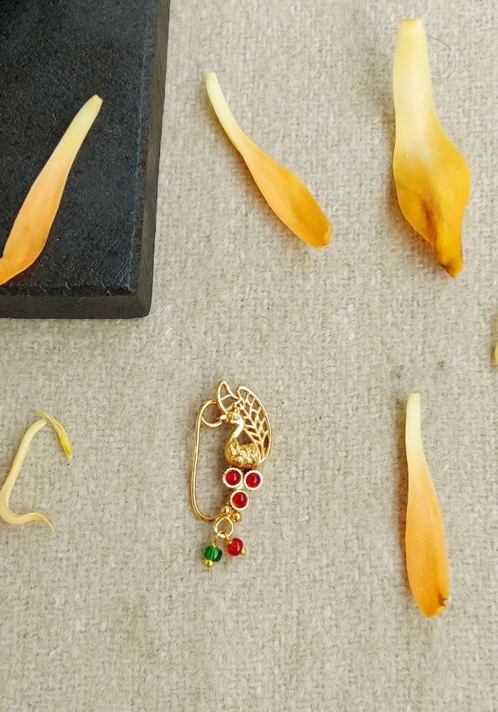 Intricate golden nath with colorful gemstones, displayed on a neutral background with scattered yellow petals.