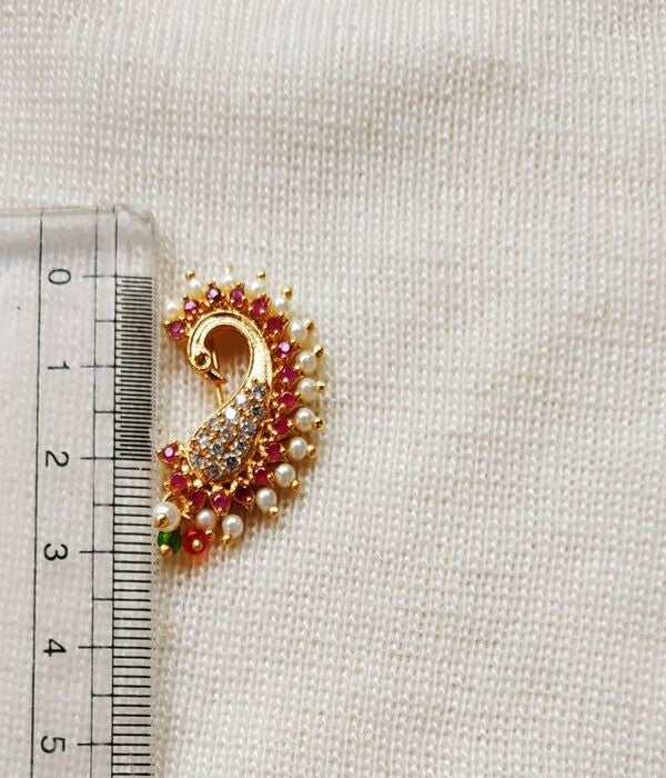 Ornate golden peacock nose ring with red and white gemstones on light fabric background