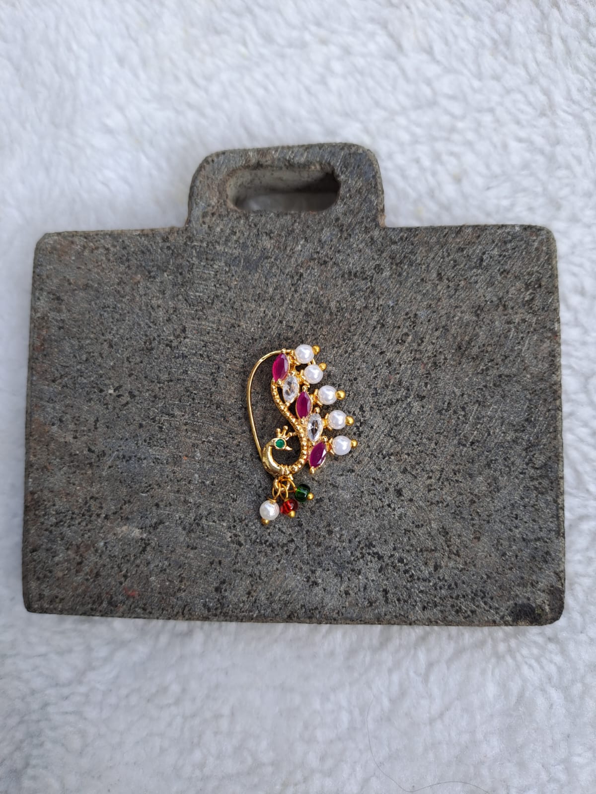 Ornate gold-toned brooch featuring a decorative design with colorful gemstones and pearls, displayed on a gray felt presentation platform.