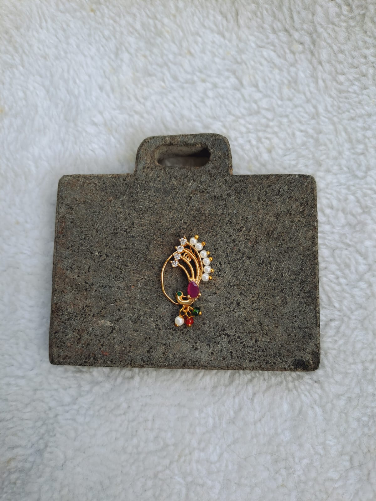 Elegant Dancing Peacock Nath - Ornate gold-toned nath (nose ring) with colorful gemstones, displayed on a dark gray fabric background.