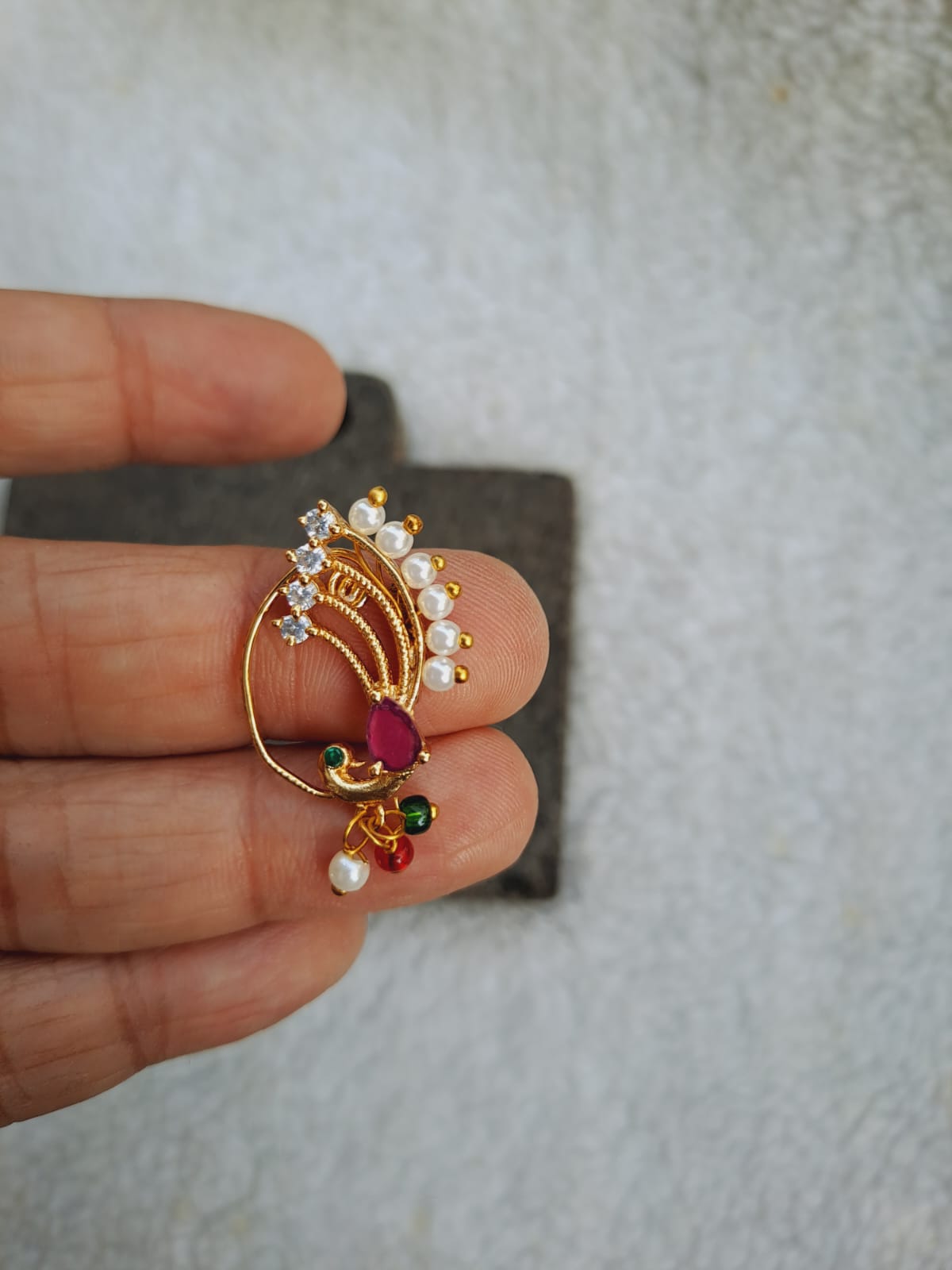 Elegant gold dancing peacock nath with pearls and colorful stones, showcased in a hand against a light background.